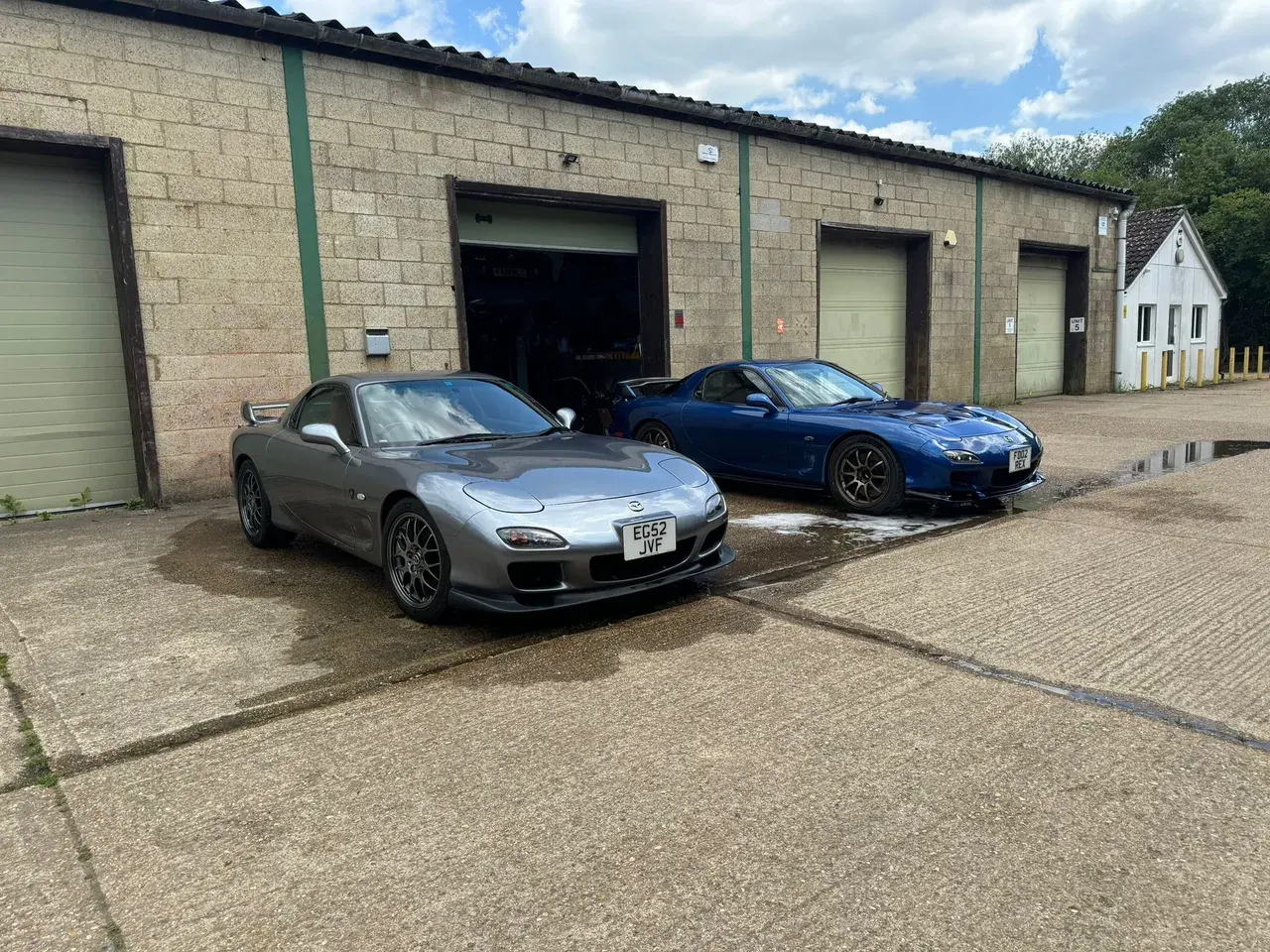Grey and blue Mazda RX-7s outside the workshop